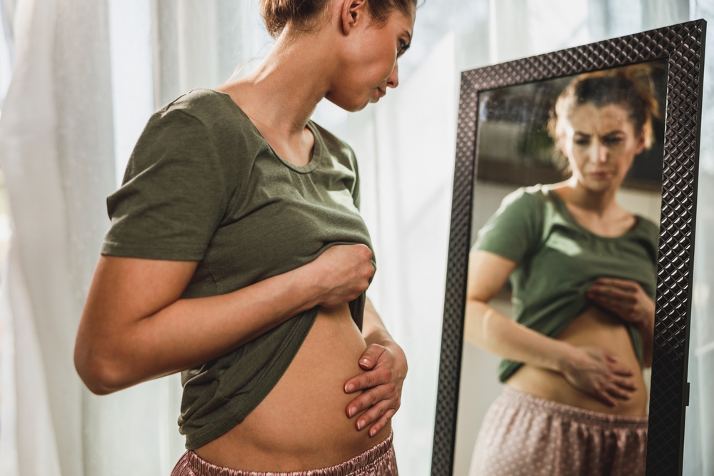 woman holding stomach looking in mirror