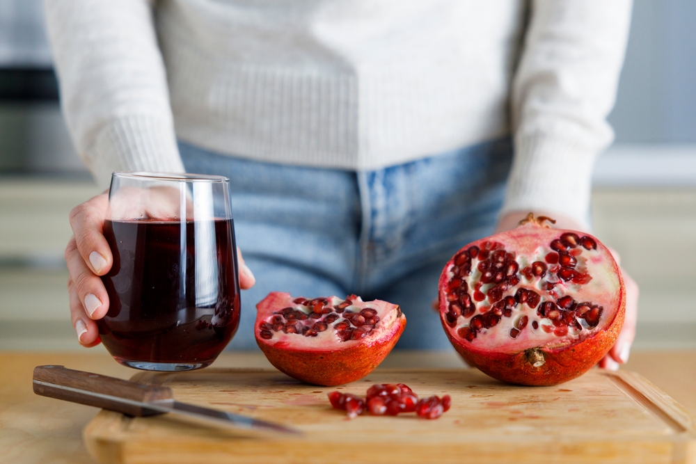 Young woman peeling a pomegranate and holding a glass of pomegranate juice.