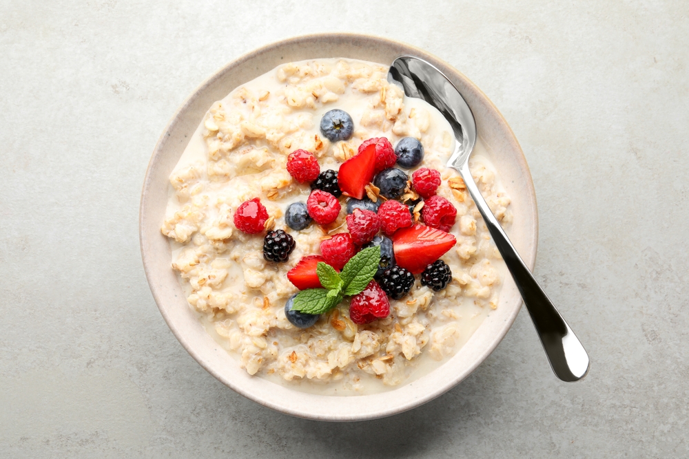 Bowl of oatmeal porridge served with berries on light grey table, top view.