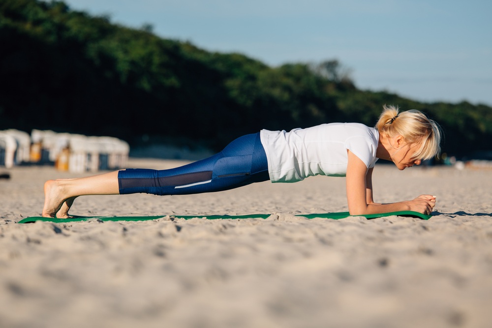 woman doing plank challenge during summer at beach