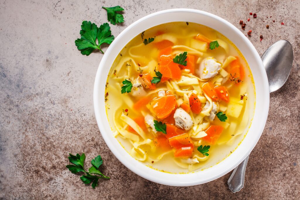 Top view of a bowl of chicken noodle soup with veggies.