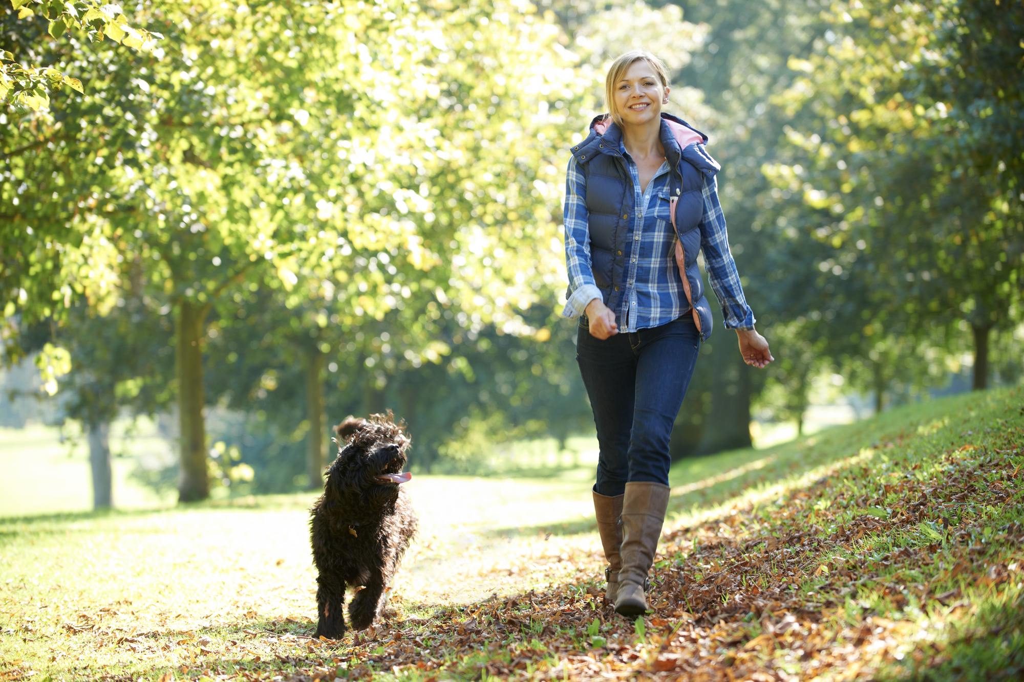 Woman walking her black dog in the park on a sunny day.