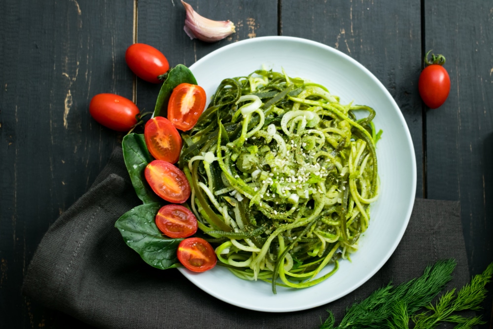 A plate of zucchini noodles topped with cheese and tomatoes.