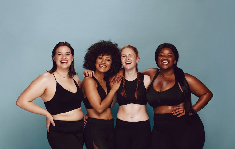 Group of women with different metabolic body types posing together in sportswear against a gray background.