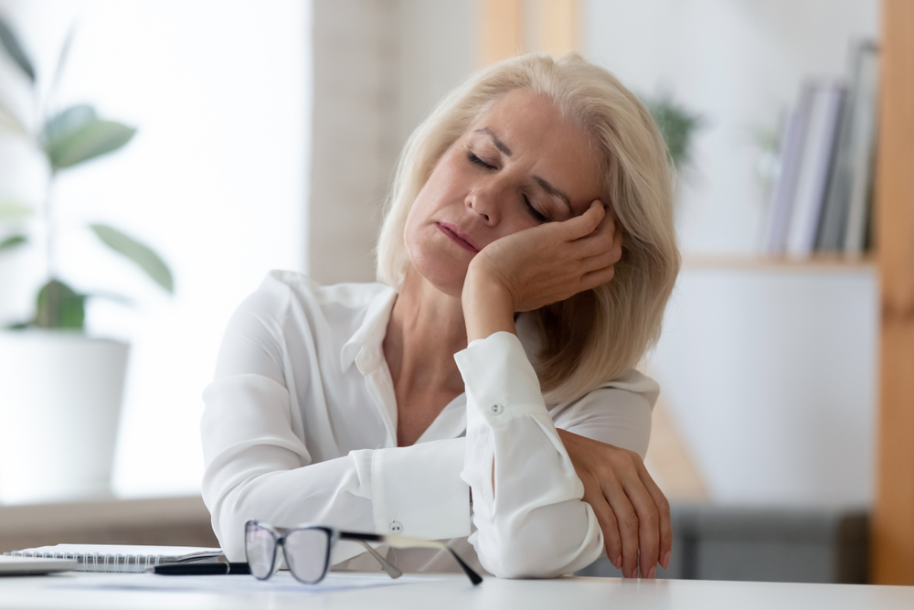 Older woman falling asleep while sitting at her desk.