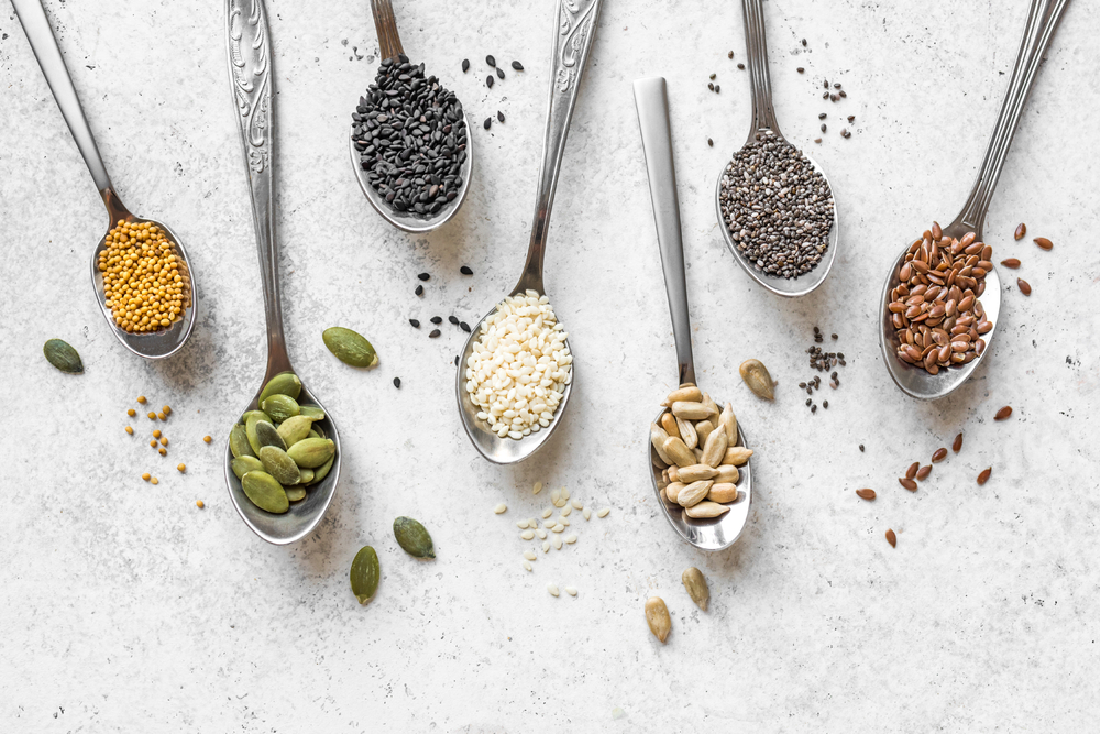 Spoonfuls of assorted healthy seeds on a white background.