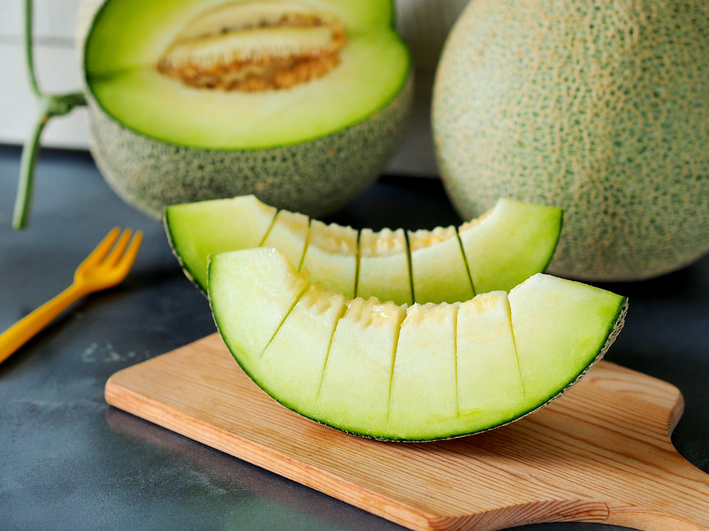 Pieces of green melon fruit or honeydew on wooden chopping board.