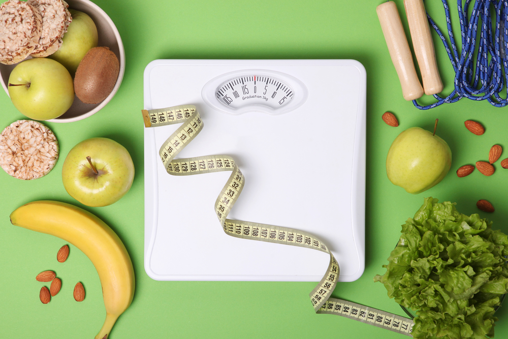 A floor scale surrounded by healthy foods and a tape measure.