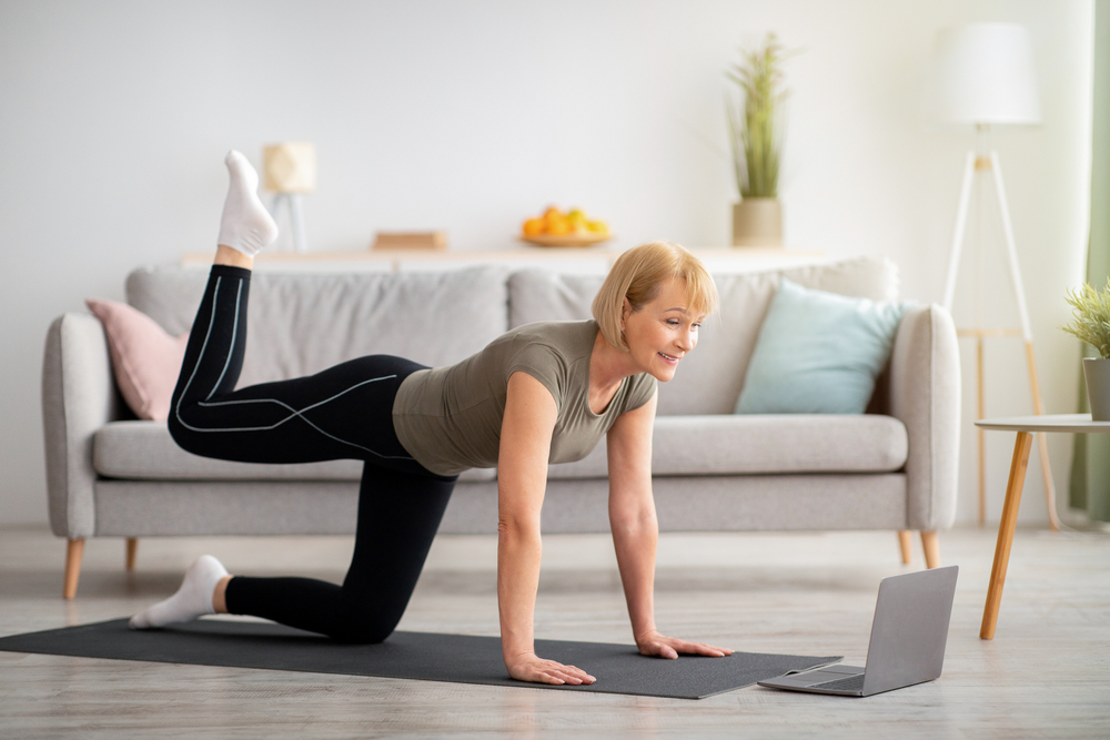 Older woman doing leg exercises on a mat in her living room.