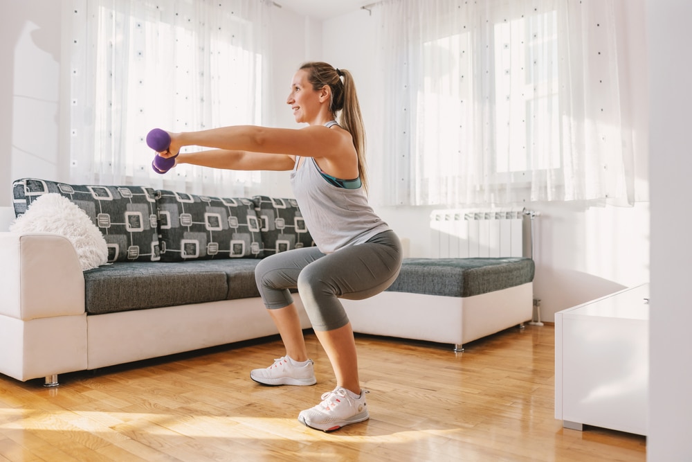 A woman doing squats with dumbbells in her living room.