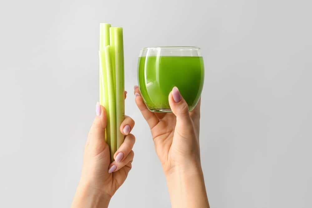 Person holding celery sticks and a glass of celery juice.