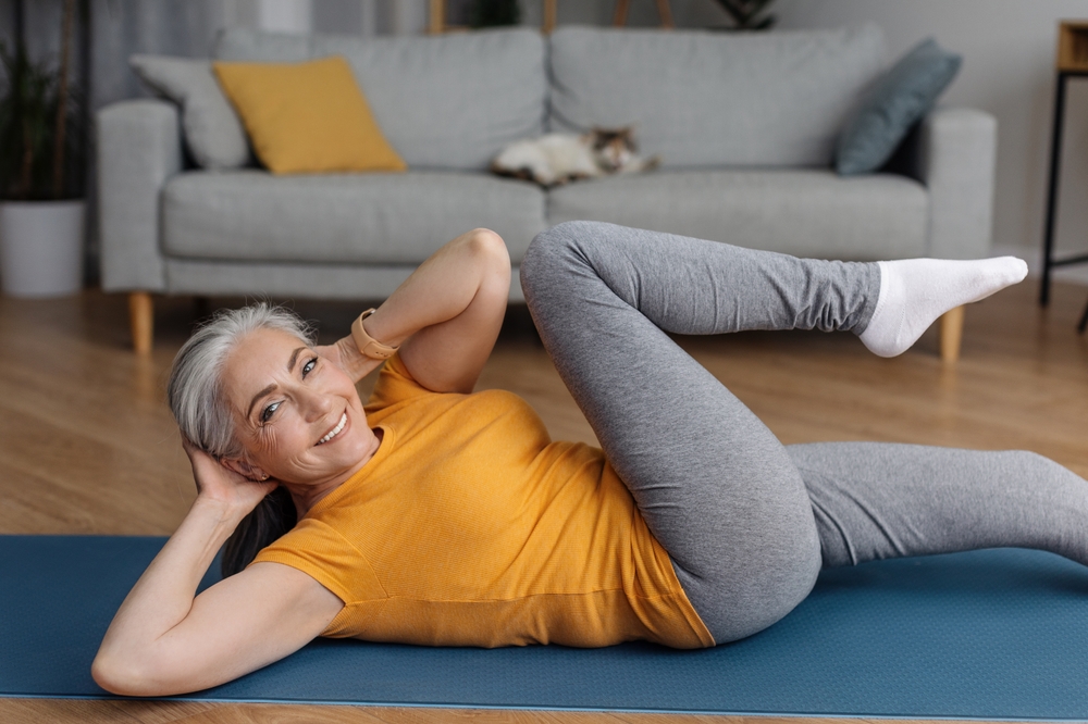 Older woman smiling while doing bicycle crunches in her living room.