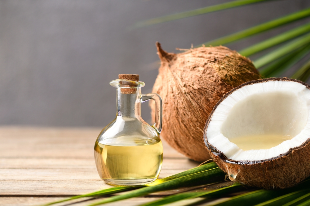 A coconut next to a small jug of coconut oil.