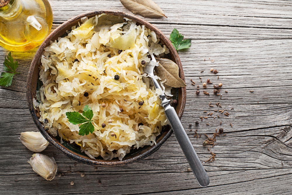 Homemade sauerkraut with black pepper and parsley in wooden bowl on rustic background. 