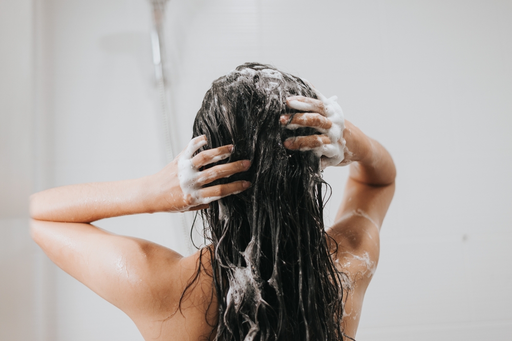 A woman washing her hair with shampoo in the shower.