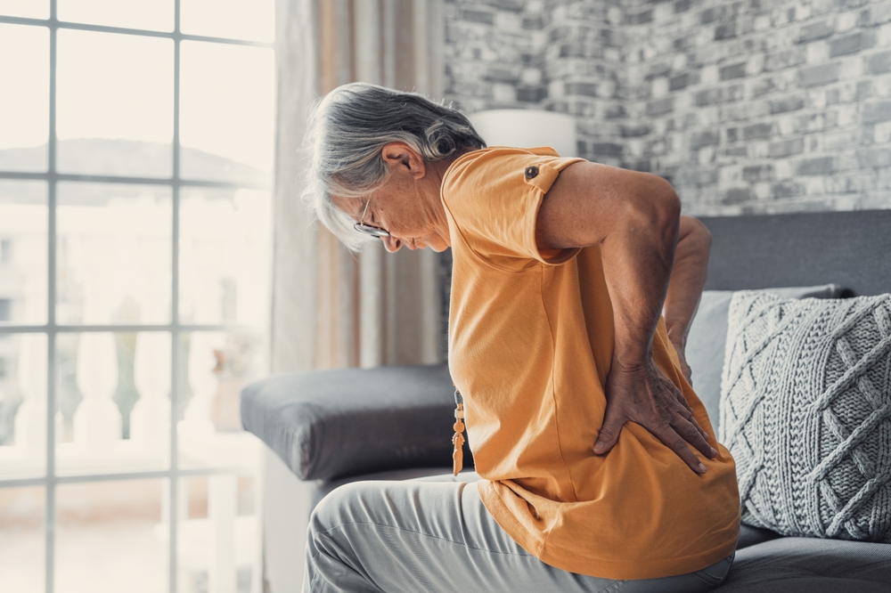 Older woman with back pain sitting on a bed.