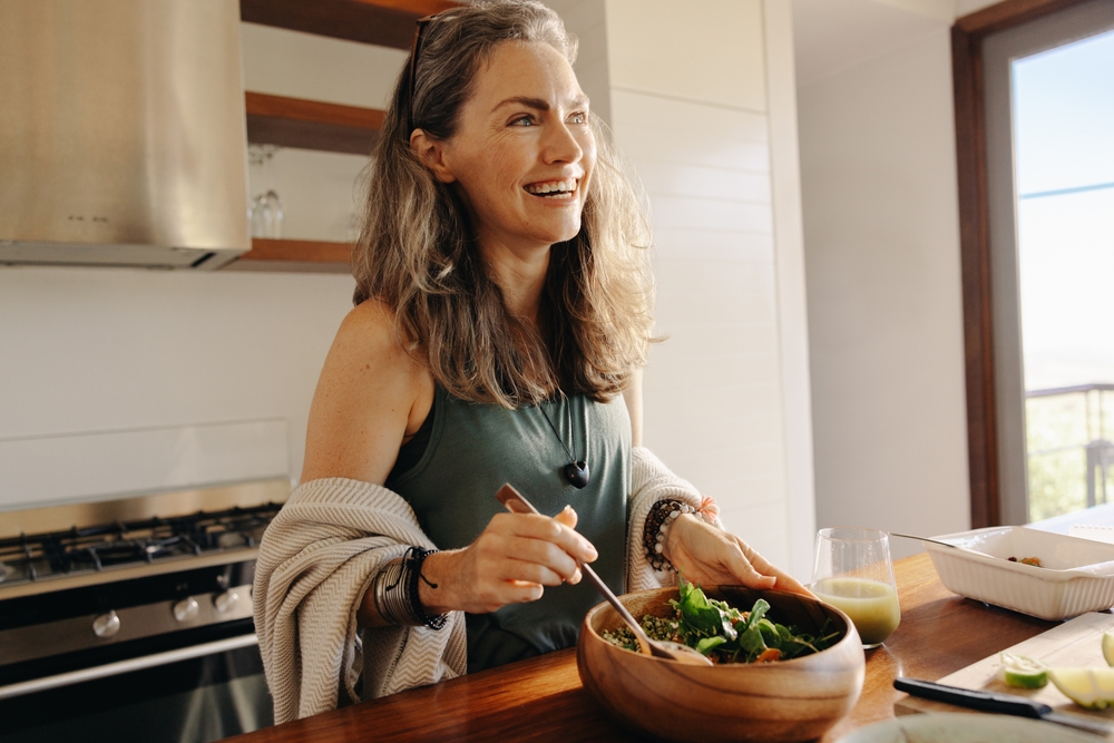 Smiling older woman eating a healthy meal in the kitchen.