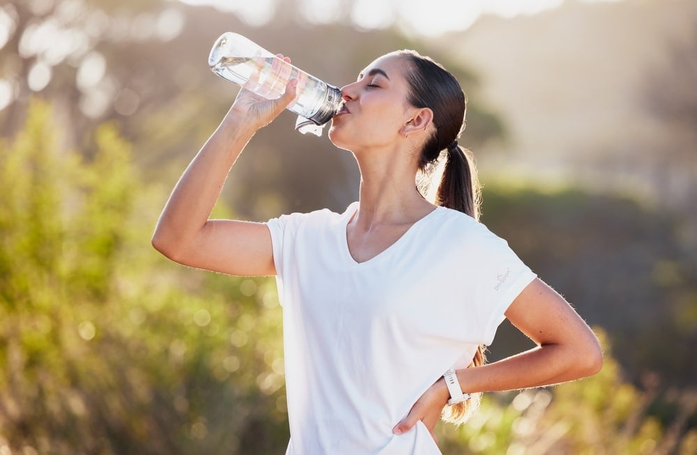 A woman drinking from a water bottle outside.