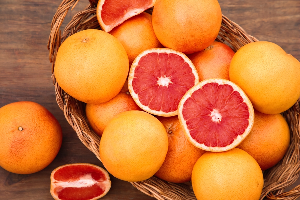 Wicker basket with fresh grapefruits on a wooden table.