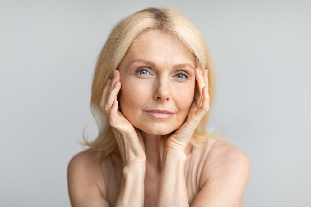 An older woman touching her face while looking straight forward.