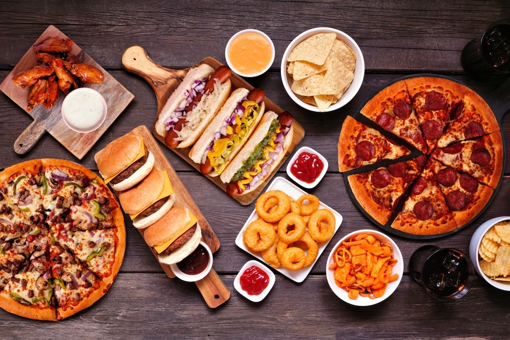 Top view of a table of junk food including pizza, burgers, and onion rings.