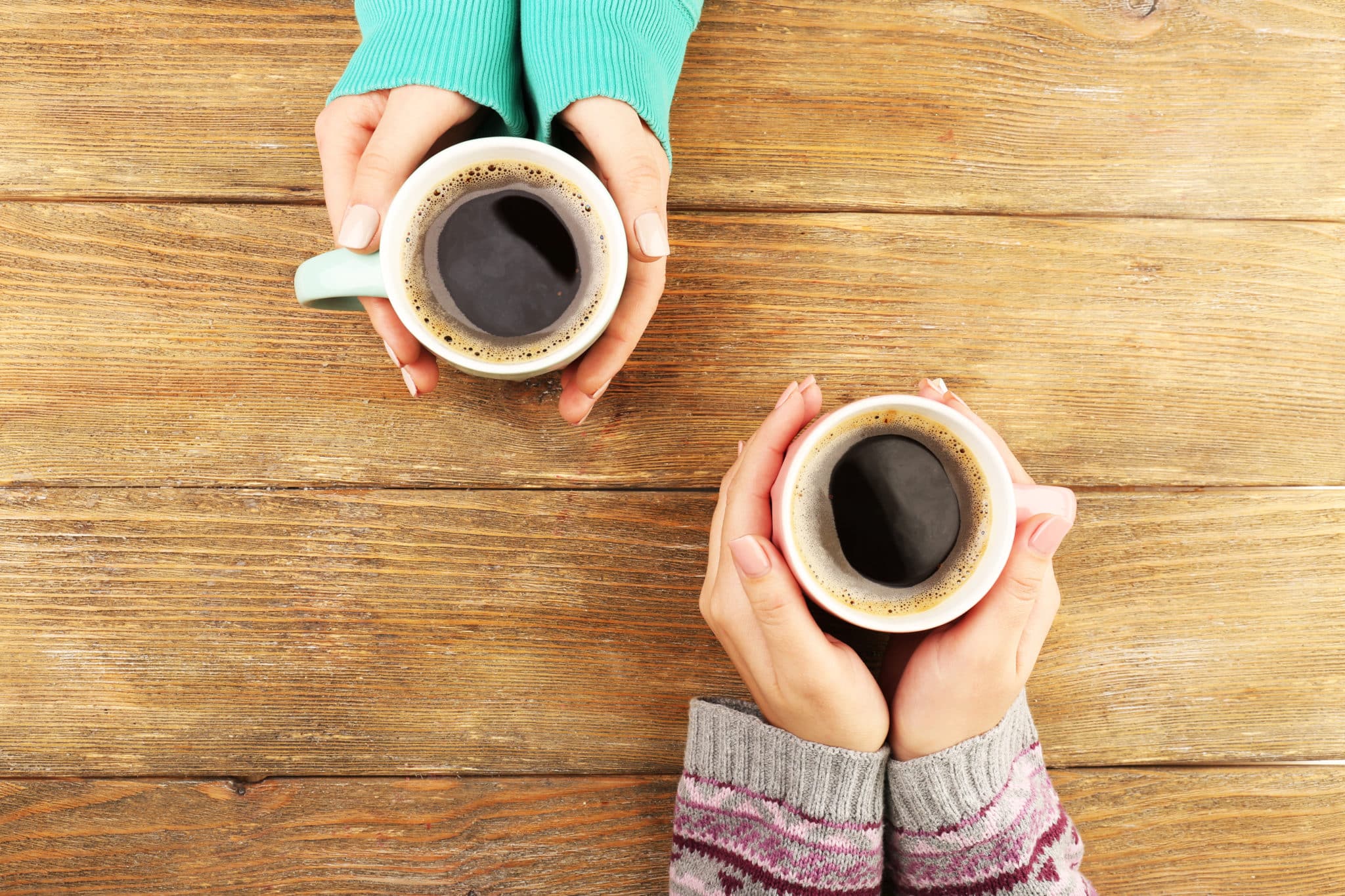 Overhead view of two people holding coffee mugs.