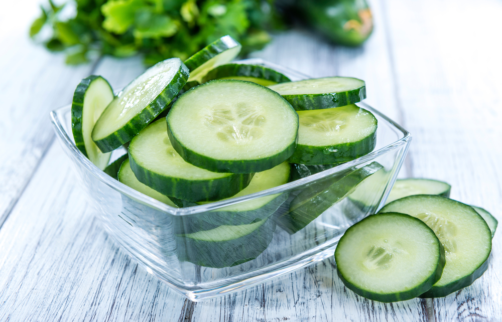 Heap of sliced cucumbers in a glass bowl on a wooden table.