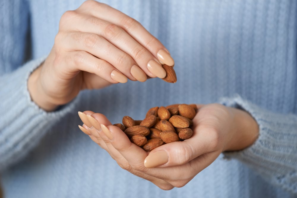 A woman holding a handful of almonds.