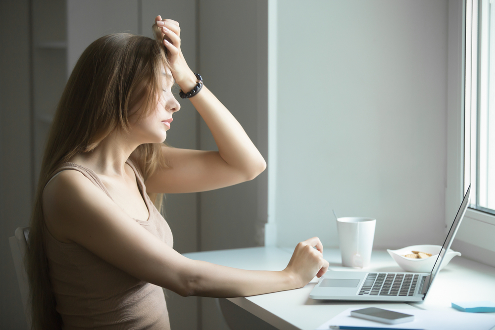 A woman with a headache sitting in front of a laptop.