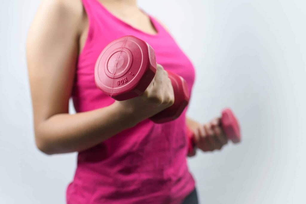 Woman in a pink tank top holding pink dumbbells.