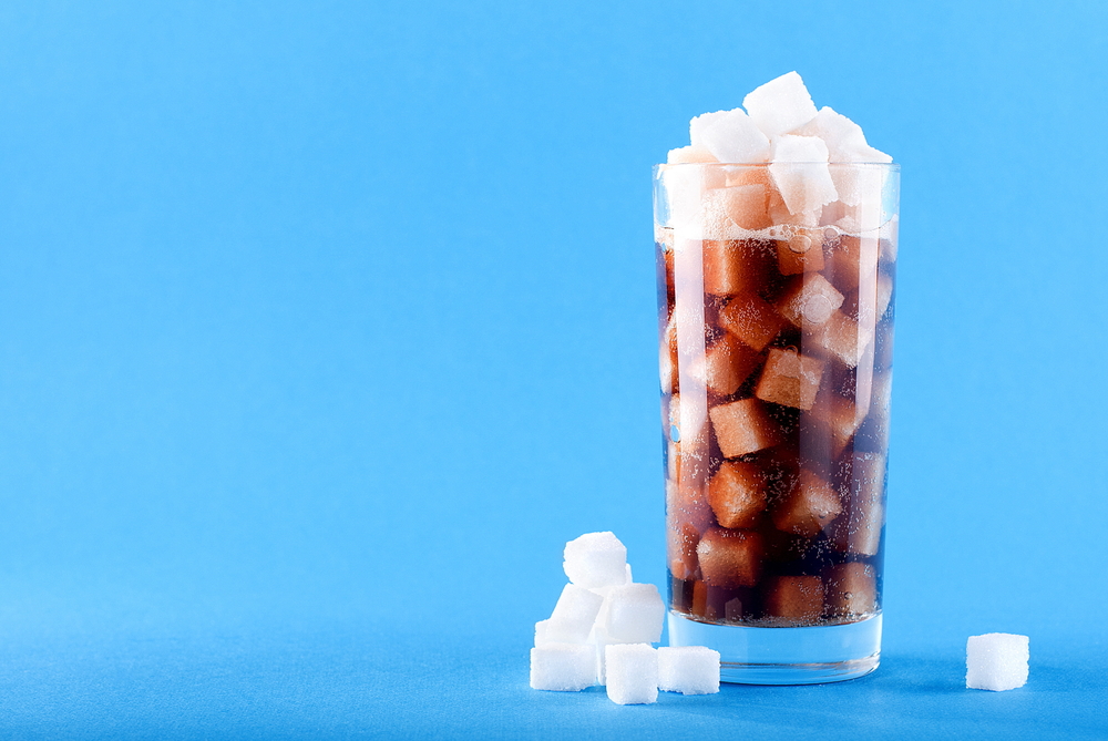 A glass of sugar cubes and soda against a blue background.