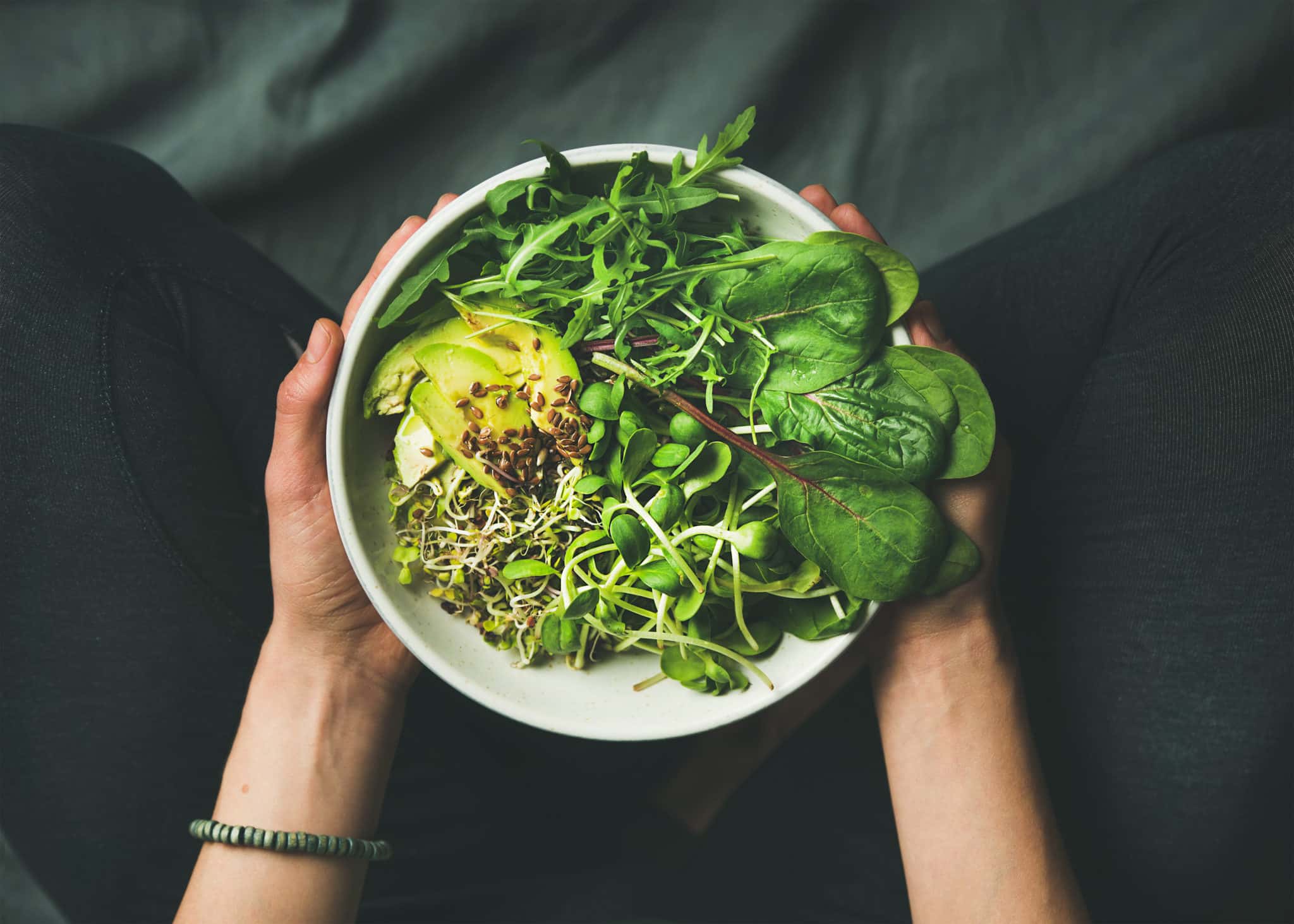 Person holding a bowl of leafy green vegetables, avocados, and other anti-inflammatory foods.