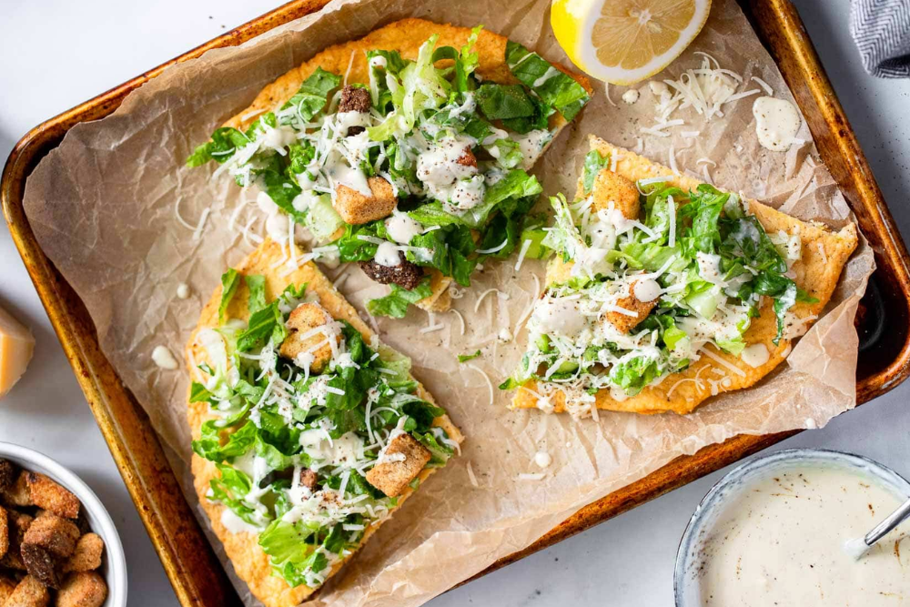 Overhead view of the viral chicken Caesar salad pizza cut into slices on a sheet pan.