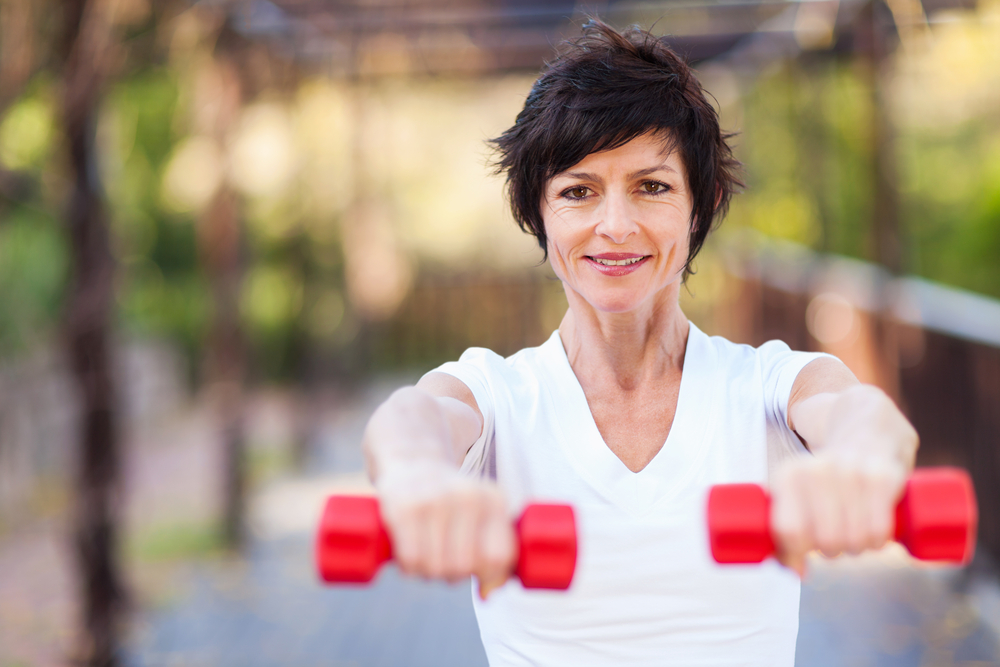 Fit older woman holding dumbells outdoors.