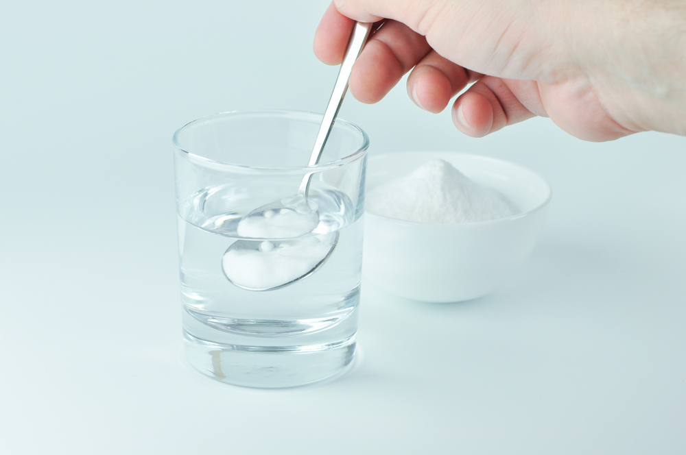 A hand mixing baking soda in a glass of water.