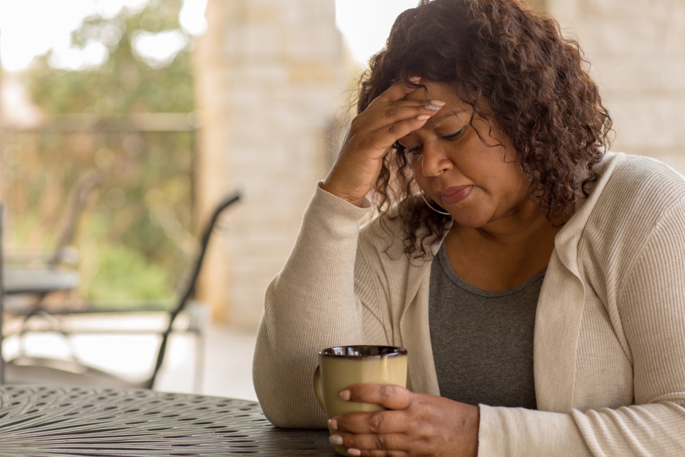 A woman sitting at an outdoor table with her hand on her head in frustratiion.