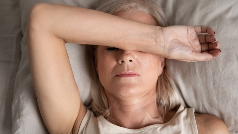 A woman lying in bed with her arm over her face.