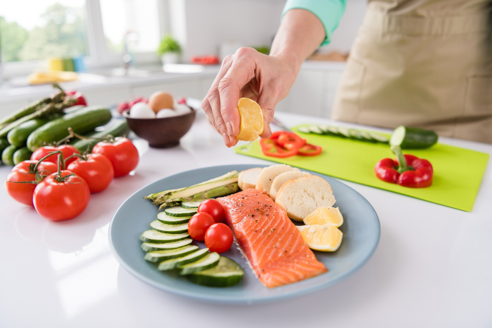 A woman adding lemon juice to a plate of salmon and veggies.