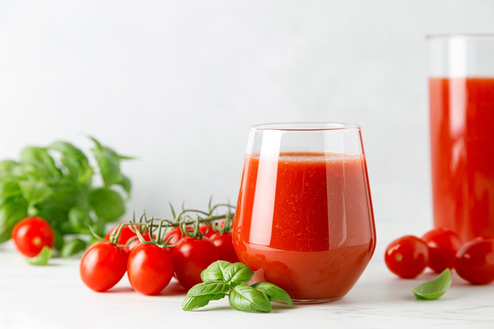 A glass of tomato juice next to small tomatoes on the vine.