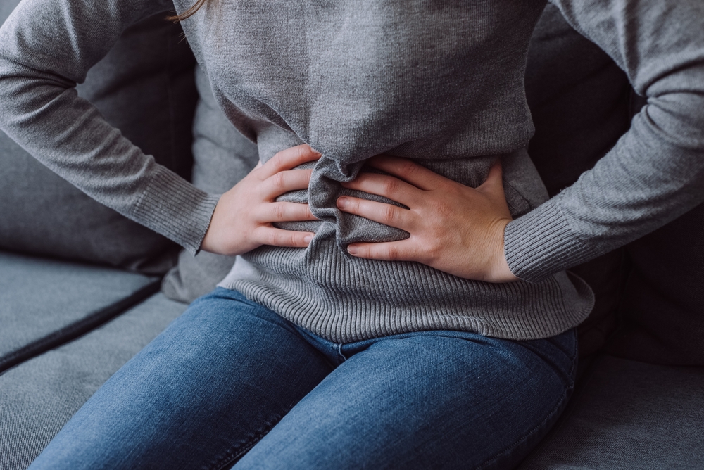 A woman sitting on the couch holding her stomach because of gas pains.