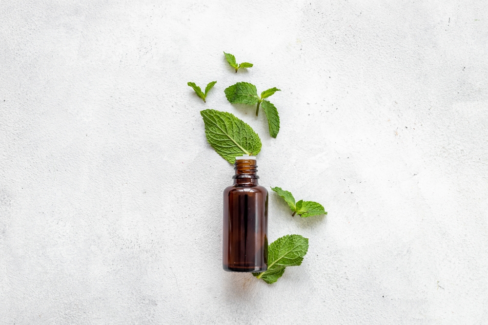 Bottle of essential peppermint oil with fresh green mint leaves.