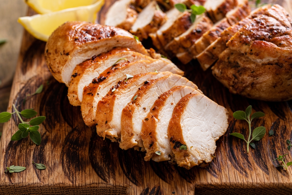 Grilled or roasted chicken breast, whole and sliced on a wooden serving plate.