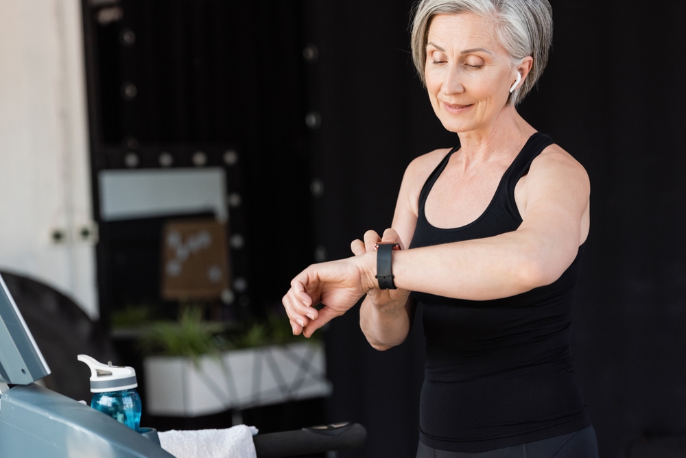 Woman with wireless headphones checking activity on fitness tracker in the gym.