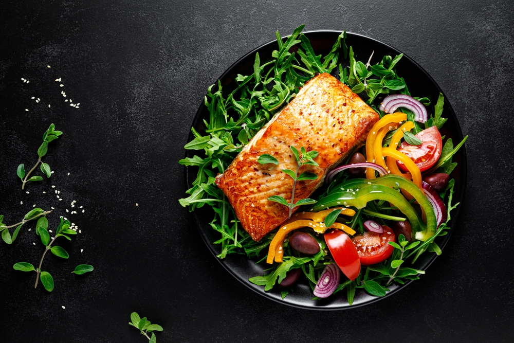 A plate of salmon, arugula and fresh veggies.