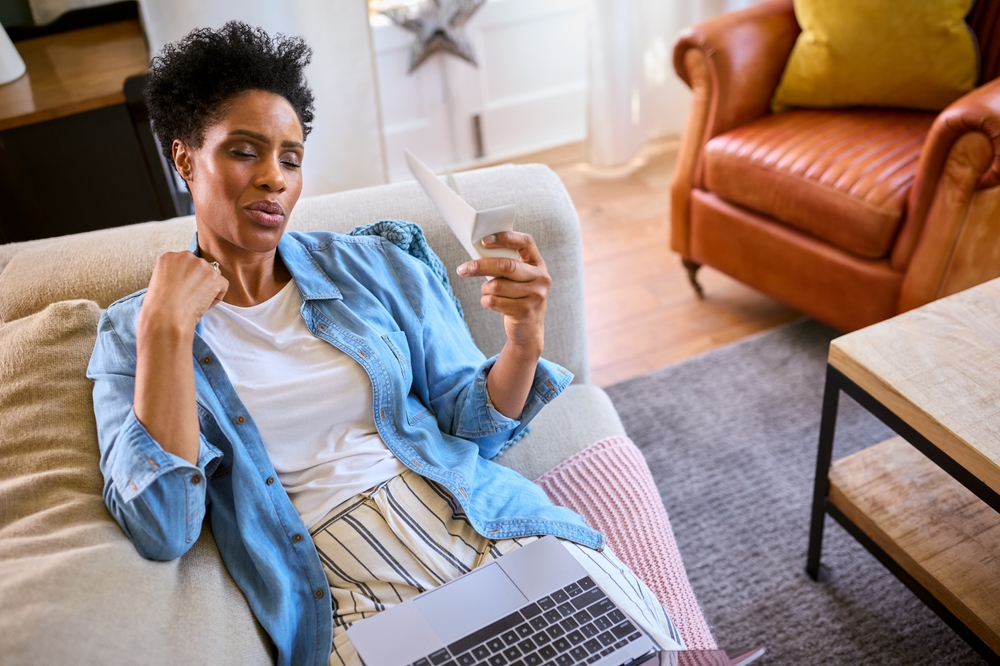 A woman sitting on the couch with her laptop having a hot flash and fanning herself.