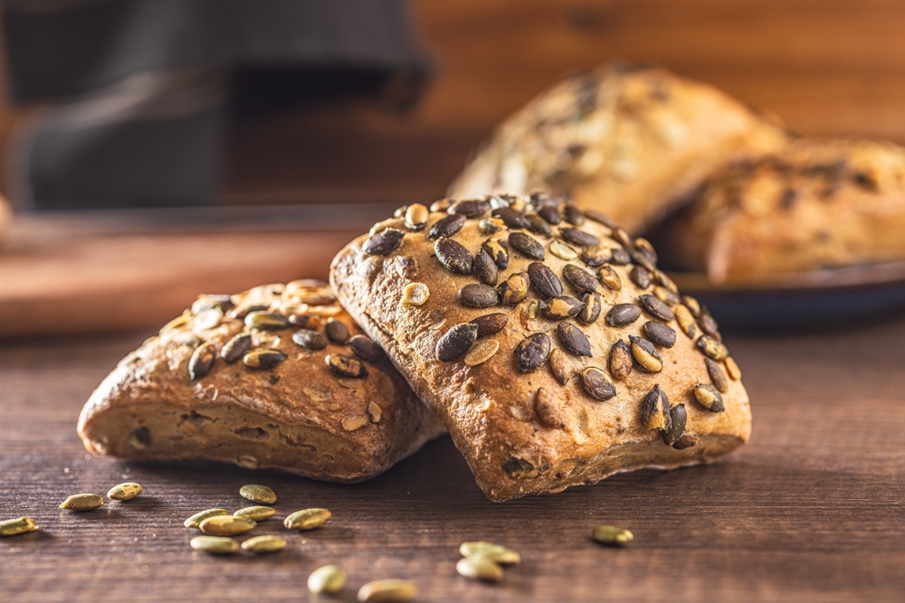 Whole grain bun with pumpkin seeds on the wooden table.