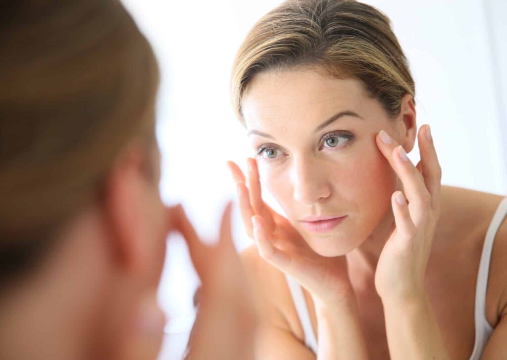 A woman examining her skin in the mirror.