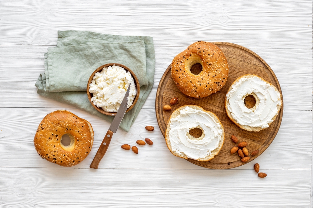 Fresh baked bagels with cream cheese on board, top view.