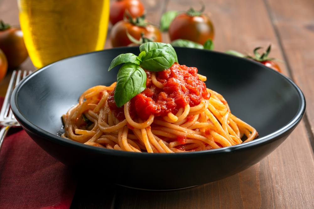 Closeup of spaghetti in a black bowl topped with marinara sauce.