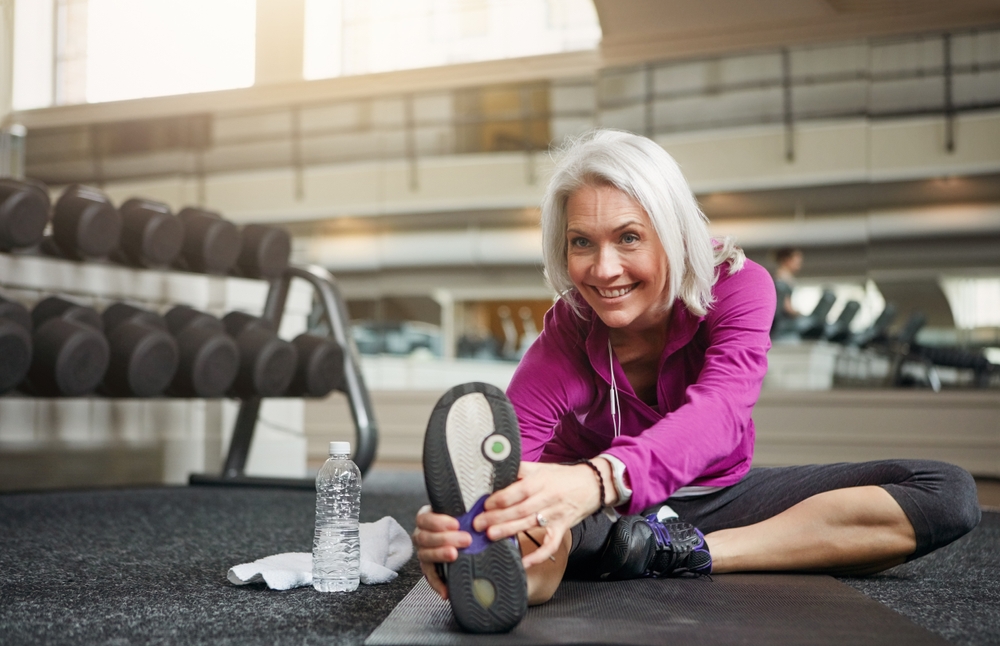 Older woman stretching on gym floor for a low-impact workout for bad knees.